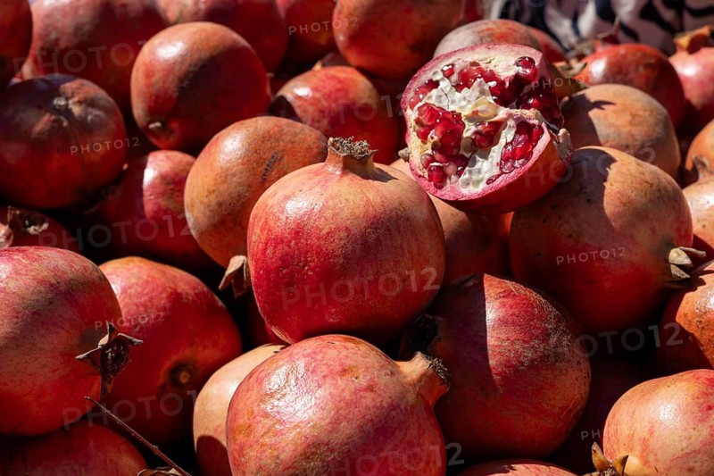 Cluster of red pomegranates, one open showing seeds, in natural light