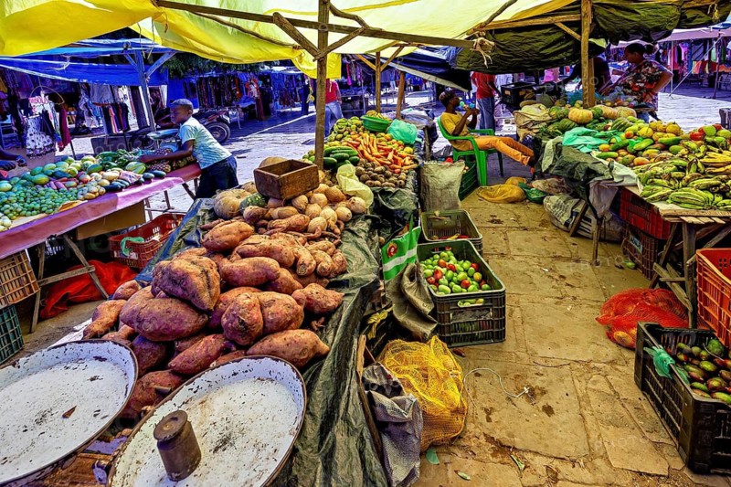 Heap of sweet potatoes and other vegetables on a busy market stand under yellow tarps, market scene in a small town in Caatinga in Bahia and Pernambuco in Brazil