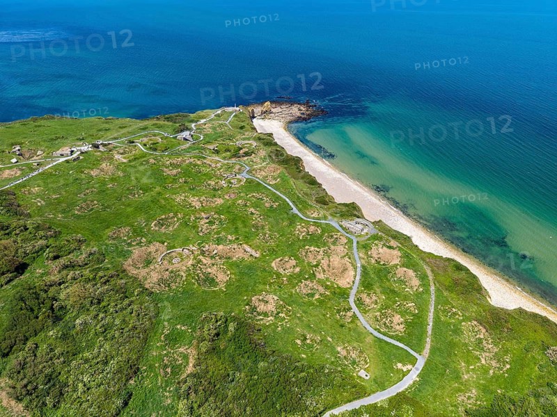 Aerial view of the historic Pointe du Hoc headland on the cliffs of Normandy. The green cliff rises prominently into the blue Atlantic. The numerous, deep bomb craters from the Second World War, which still shape the landscape today, are clearly visible. At this former base of the German Wehrmacht, a decisive battle took place on June 6, 1944 during the Allied Invasion, D-Day, Operation Overlord, Omaha Beach, Calvados Department, Normandy, English Channel, France