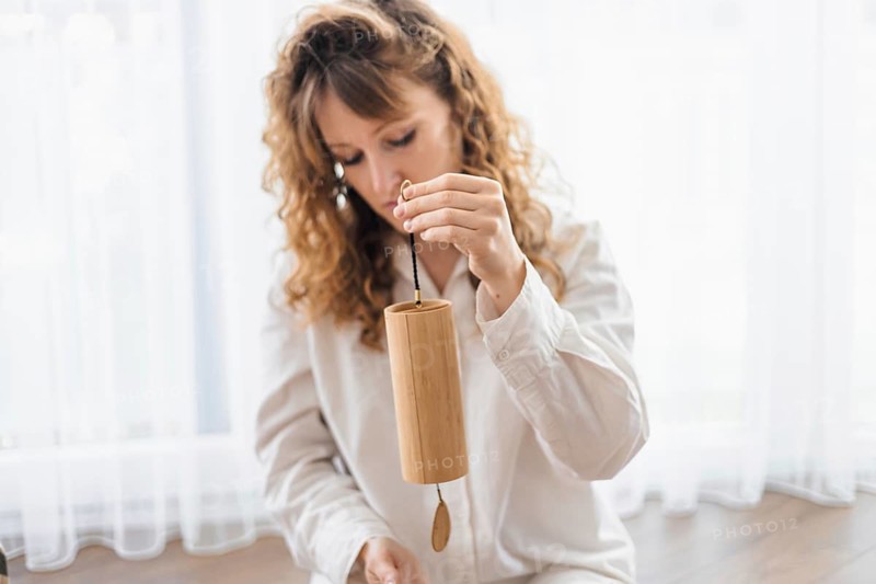 A woman seated, gently holding a wooden chime in a peaceful setting