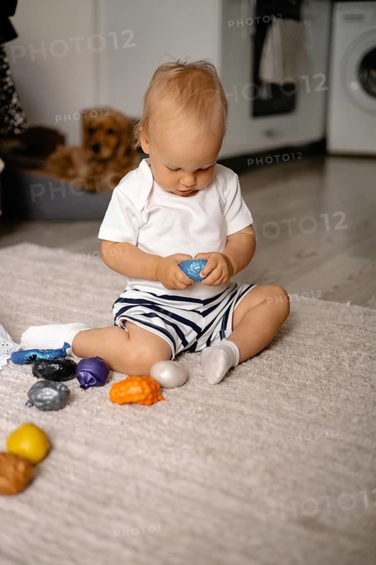 Baby concentrating on a blue toy while seated on a rug