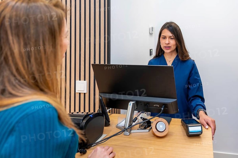 Professional receptionist assisting a client at a modern wooden front desk in an elegant aesthetic clinic, managing appointments and payments with friendly, efficient customer service