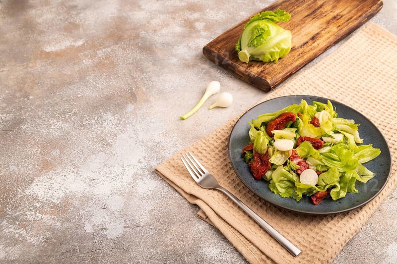 Mixed salad with lettuce, tomatoes, onion and vegetables on blue plate on brown concrete background and beige textile. side view, copy space