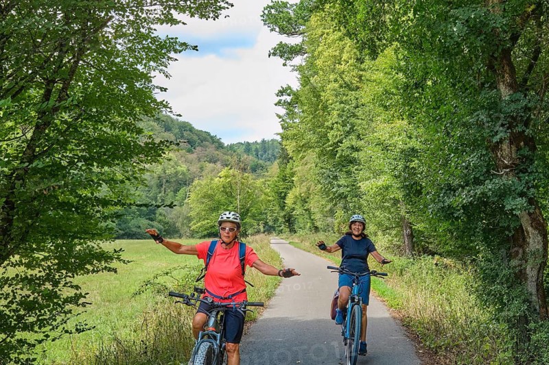 Active senior girlfriends having fun practicing handsfree cycling on a bike path through a peaceful forest, showing balance, confidence, freedom and active aging