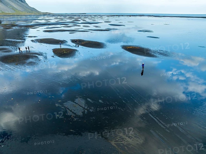 Aerial view of black lava beach at Mt. Vestrahorn, people on the beach, clouds are reflected on the water, Stokksnes, east of Höfn, East Fjords, Iceland