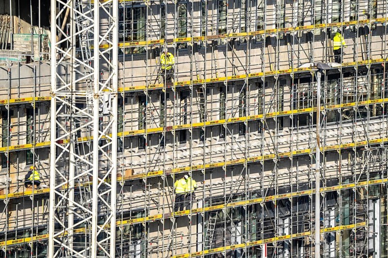 Large construction site, scaffolded new building, factory and office building, workers on the scaffolding during facade work