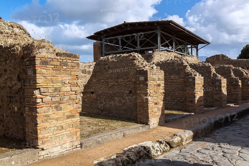 Old terracotta brick and stone building structures and walls plus street surface made of large grey smooth and worn lava stones at the ancient ruins of Pompeii, Campania region, Italy
