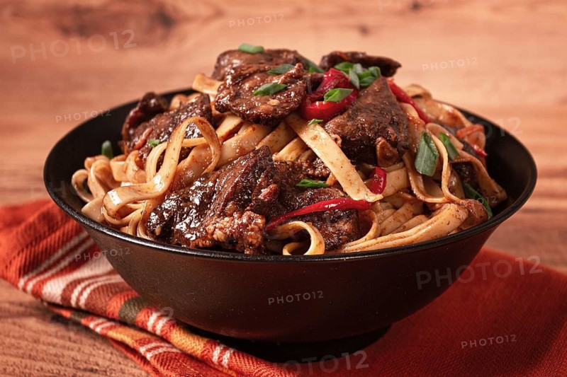 Udon noodles with beef in Mongolian style, with green onions and vegetables, served in a black bowl, on a wooden table, homemade, no people