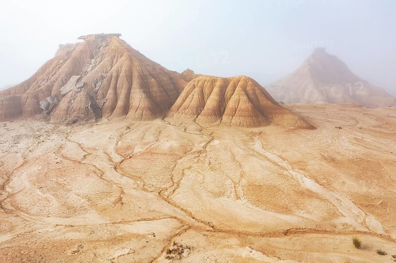 A serene desert landscape features eroded hills cloaked in a soft mist The golden earth and intricate rock formations create a sense of mystery and solitude