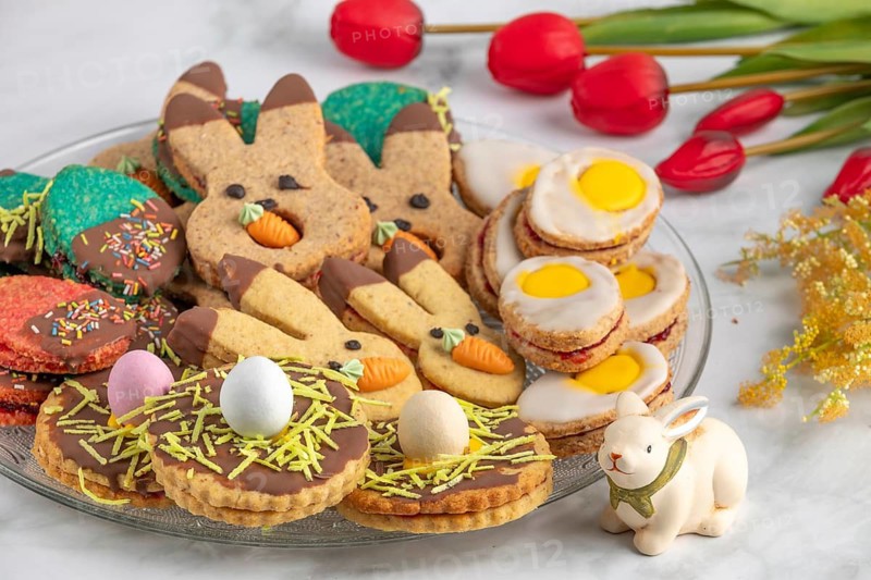 Plate of colourful Easter biscuits, decorated with carrots and eggs, next to red tulips