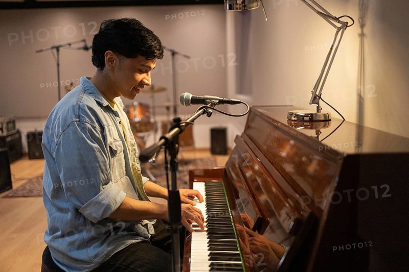A musician plays the piano in a cozy recording studio, surrounded by microphones and equipment. The warm lighting creates an inviting atmosphere for creativity