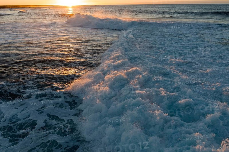 Waves crash energetically at Popcorn Beach in Fuerteventura during a picturesque sunset, creating a dynamic ocean view against the glowing horizon