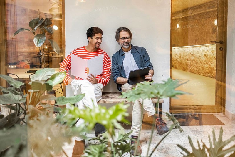 Two professionals enjoy a relaxed outdoor meeting in a modern coworking space surrounded by lush greenery, emphasizing collaboration and creativity