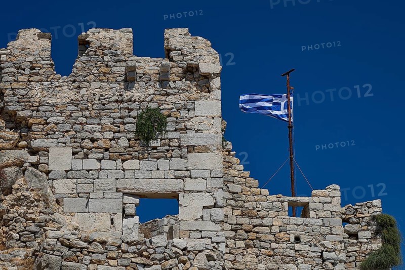 Old stone ruins with a waving Greek flag against a deep blue sky, Johanniter fortress from the 14th century AD, fortress of Megalo Chorio, Kastro, Megalo Chorio, Zero Waste Island, Tilos, Dodecanese, Greek Islands, Greece