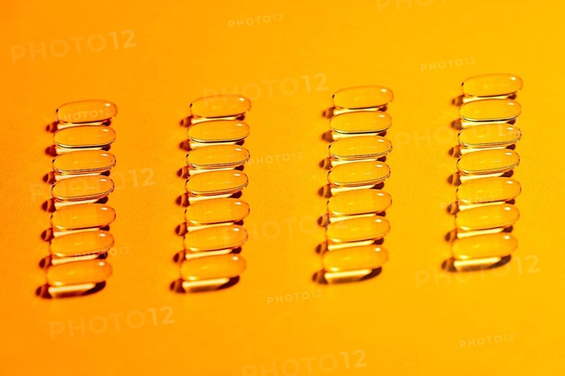 The image showcases multiple rows of clear, oval shaped capsules meticulously arranged on a striking yellow background, offering a vivid, uniform aesthetic