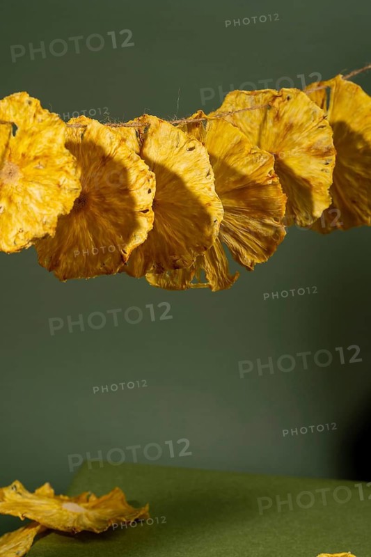 A close-up shot of beautifully dried pineapple slices arranged in a row against a muted green backdrop, showcasing the texture and rich yellow hues of the fruit
