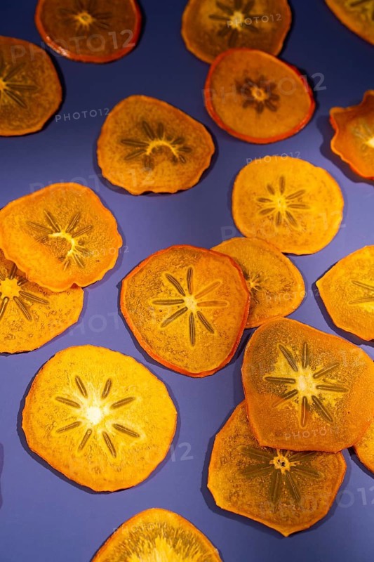 Brightly lit, translucent slices of dried persimmon arranged artistically on a vivid purple background, showcasing their unique star-like patterns