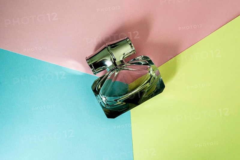 Bottle of perfume on the background of yellow, pink and blue. Top view. Copy space, A modern glass perfume bottle rests on a colorful, geometric background of blue, pink, and yellow