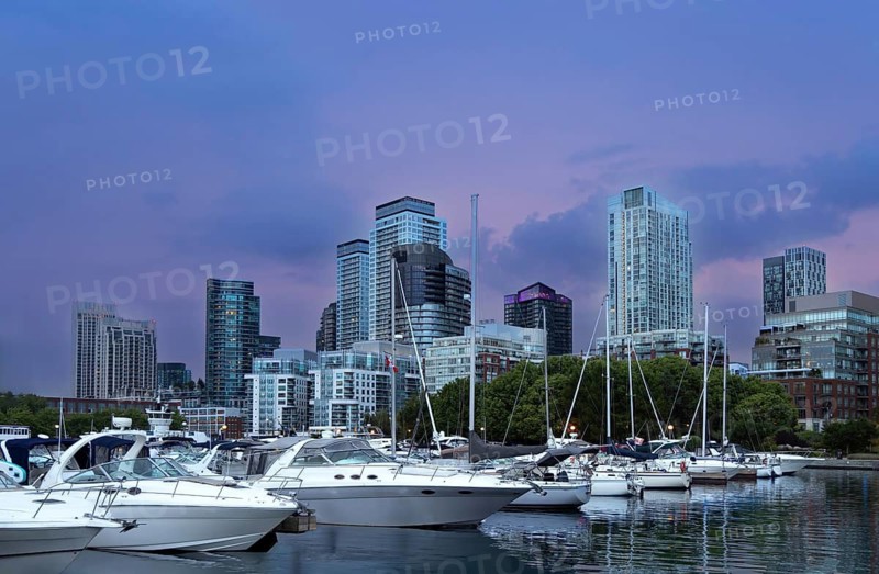 Yachts and sailboats moored at a harbour marina with high rise skyline buildings and skyscrapers under a sunset sky near downtown and Toronto Islands