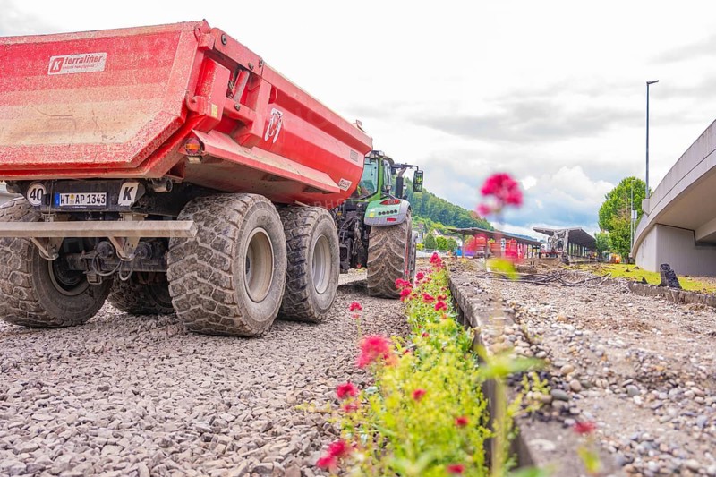 Large construction truck lined with blooming flowers on gravel road, Leonhard Weiß electrification station conversion, Waldshut. germany