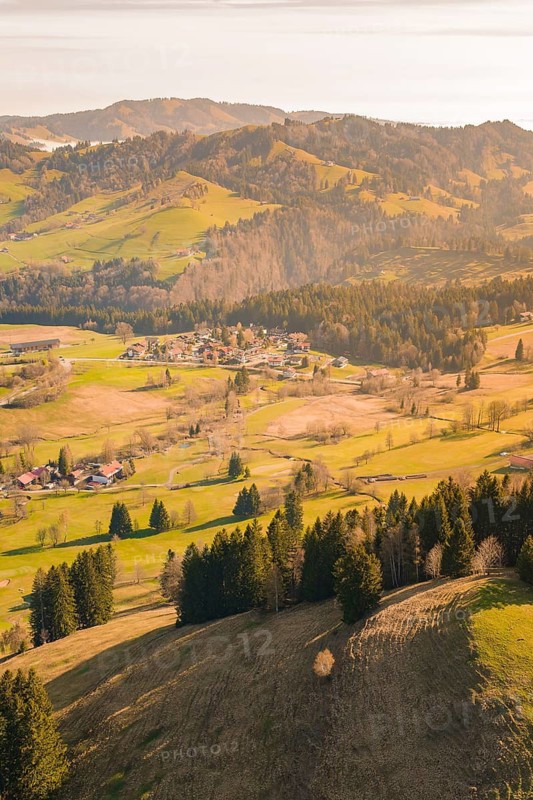 A panoramic view of a village between green hills and wooded mountains, Allgäu, Bavaria, Germany