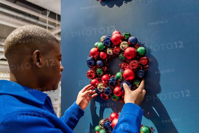 A close-up on a man's hand placing a garland on a blue wall. Christmas wreath has red, green balls