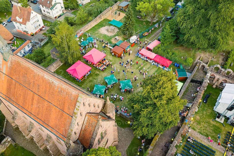 Bird's-eye view of summer party with colorful tents, crowds and green surroundings, Calwer Klostersommer Festival, Hirsau Abbey, Calw, Germany