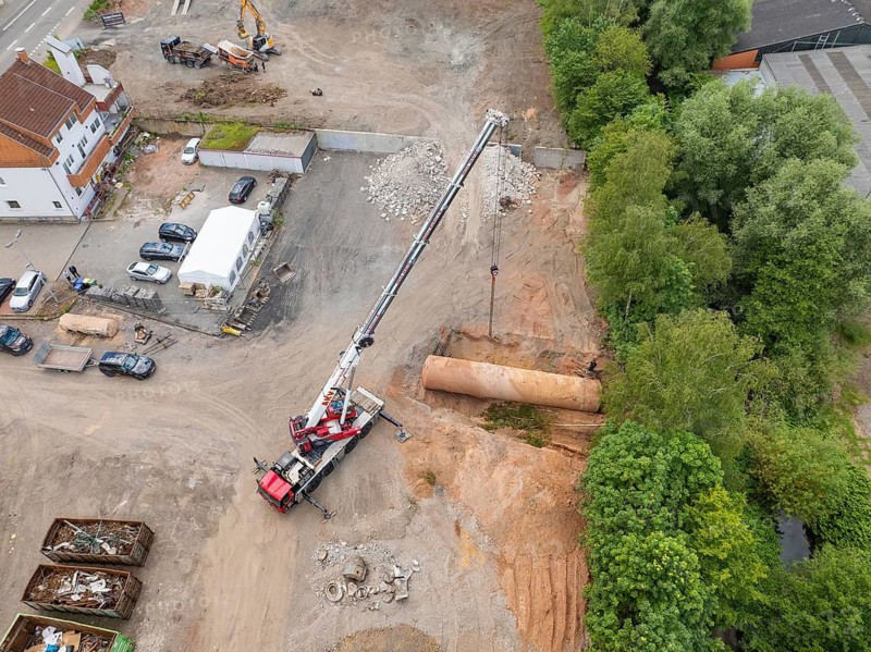 Aerial view of a construction site with a crane moving material, surrounded by trees and houses, demolition site of a former lorry haulage company with oil tanks, Saarbrücken, Germany
