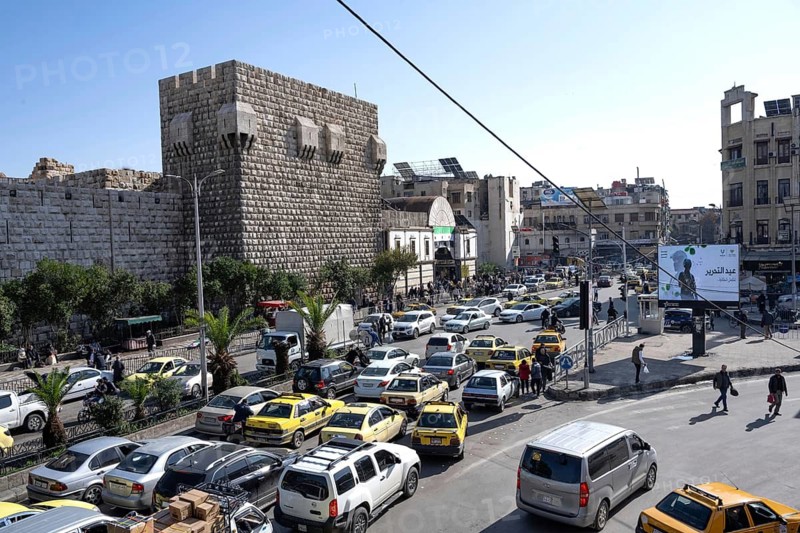 Damascus, Syria. December 7th 2025. Syrian streets busy with traffic in front of the ancient walls of Damascus Citadel and the entrance to Souk al Hamadiyeh, Damascus Old City, Syria