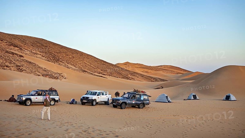 Desert camp in daylight with tents and off-road vehicles in front of sand dunes, adventure camping with off-road vehicles in the Sahara desert in Algeria