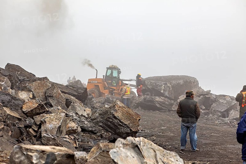 Excavator picks up large rocks on foggy construction site, workers nearby, rock slide on the pass road towards Rurrenabaque through the Andes on the road of death in Bolivia