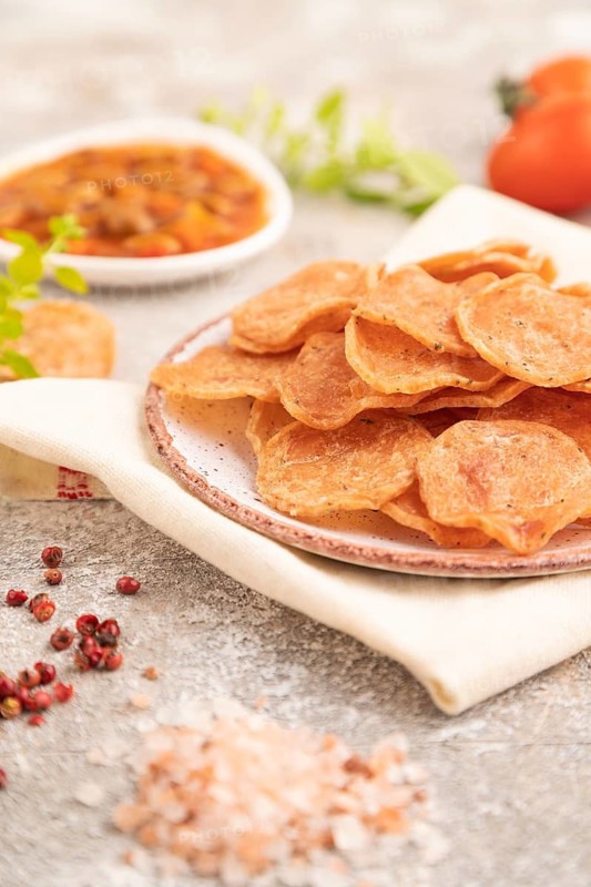 Slices of dehydrated salted meat chips with herbs and spices on gray concrete background and white textile. Side view, close up, selective focus