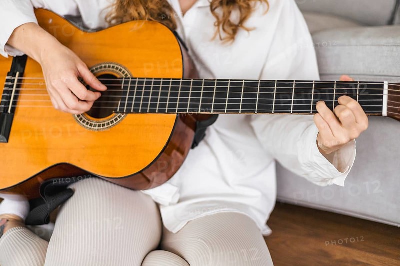 Person playing an acoustic guitar in a relaxed setting with focus on hands and instrument, creating a cozy atmosphere