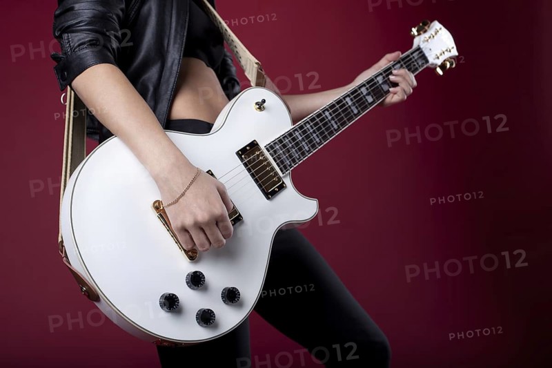 Sexy rock woman in black leather posing with electro guitar on red background