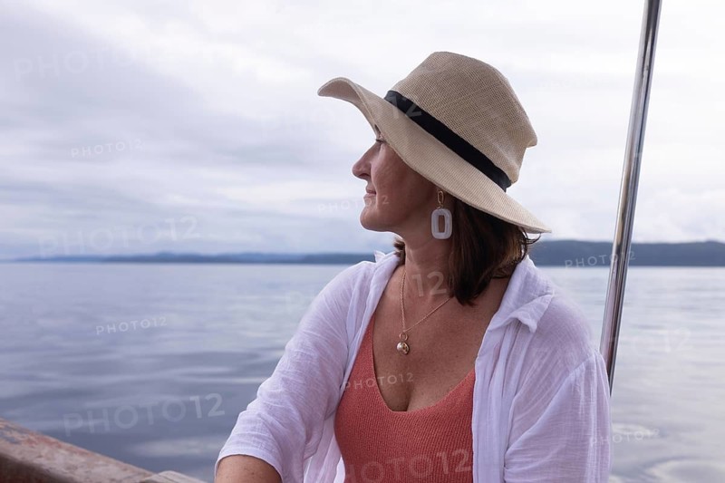 A mature woman tourist wearing a sun hat gazes out over the sea at a homestay on Kri Island, in the Raja Ampat Archipelago, West Papua, Indonesia