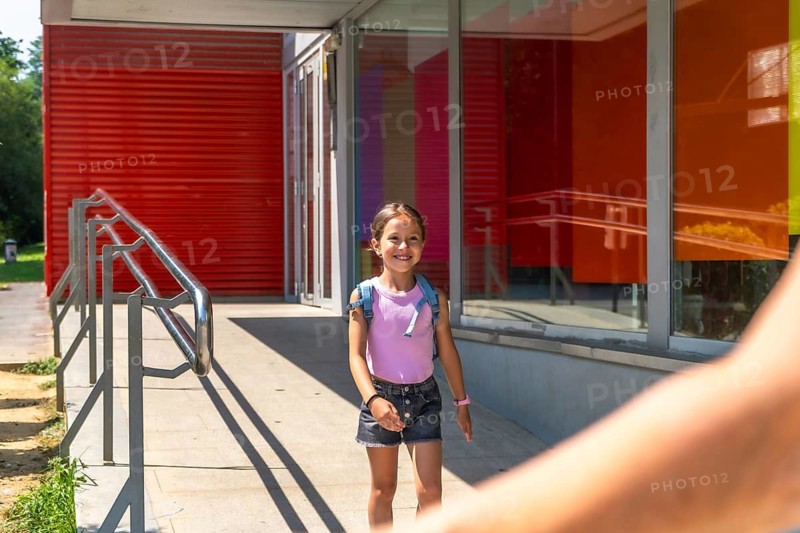 Young girl smiling and walking out of school after class, holding an adult's hand, embodying childhood education, family pick up, and everyday family life togetherness