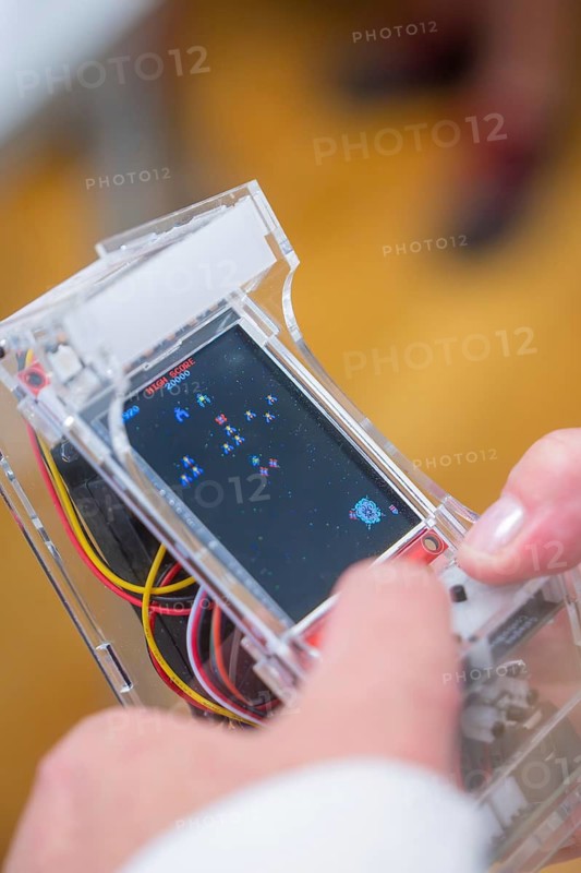 A person holds a transparent handheld console with an arcade game running, Youth Research Center, Nagold, Germany