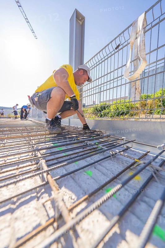 Construction worker in yellow T-shirt working on metal reinforcements on a construction site in sunny weather, parking garage construction, Calw, Germany