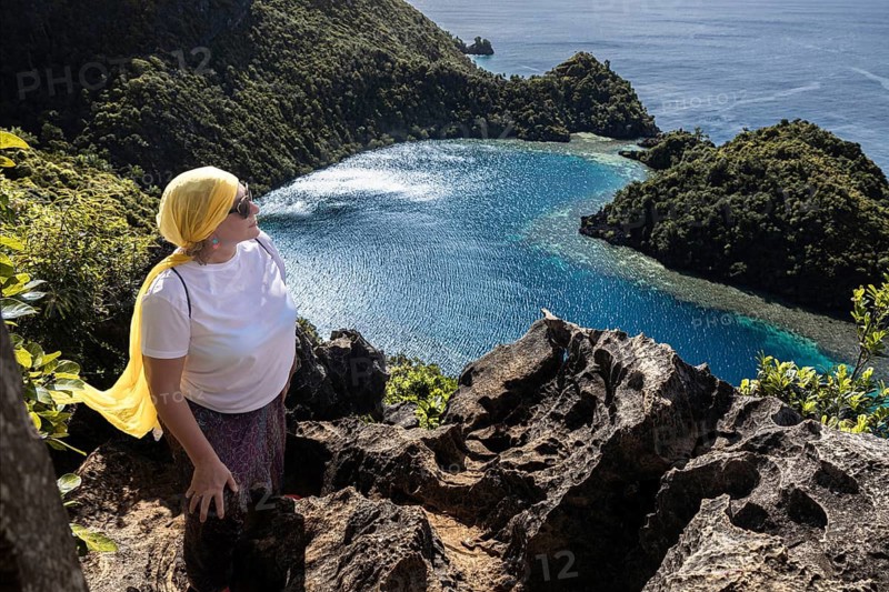 A female tourist enjoys the stunning view of the blue waters and lush islands of Raja Ampat, Indonesia. The vibrant landscape enhances the area's natural beauty