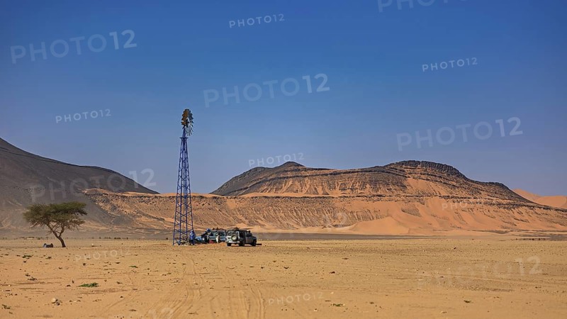 Desert landscape with wind turbine, off-road vehicle and tree under a clear blue sky, water pump in the Sahara in Algeria