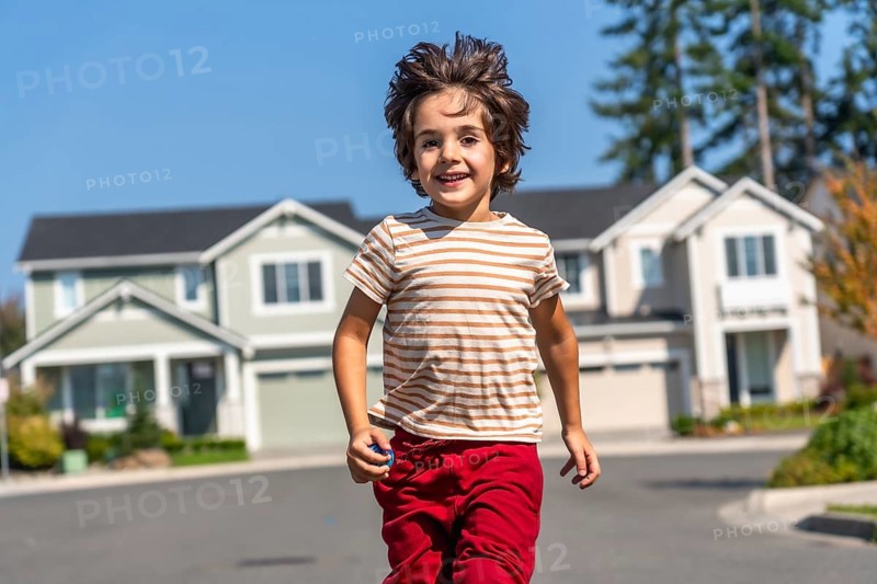 Young boy enjoying childhood, running and smiling towards the camera on a sunny day in a peaceful, residential street with houses in the background