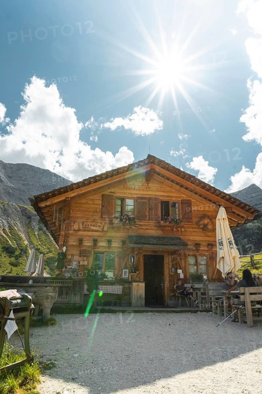 Dolomites, Italy - 15th july, 2025: Rustic wooden mountain hut chalet with restaurant terrace blue sky bright sunburst lens flare background Malga Rossalm loop trail Dolomites South Tyrol Italy summer travel