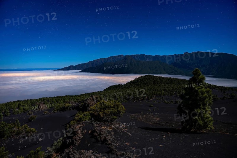 View from Mirador Astronómico del Llano del Jable of the Caldera de Taburiente National Park and a sea of fog. At night The lights of El Paso shine through the clouds. La Palma, Canary Islands, Spain