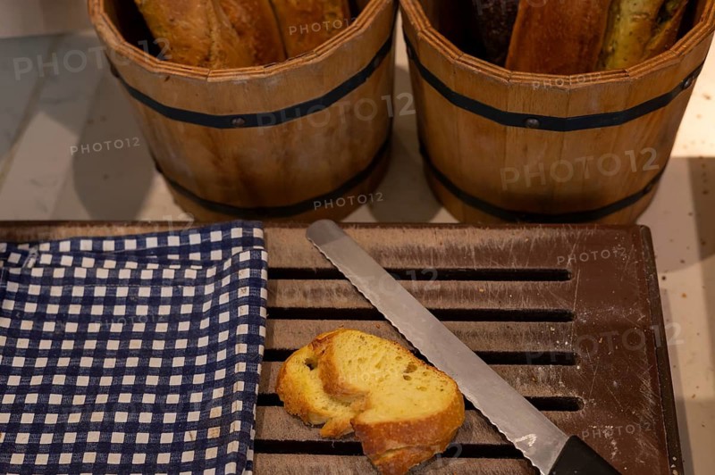 Sliced bread rests on a wooden cutting board next to a knife, with baskets of whole loaves in the background. Homemade freshly baked bread