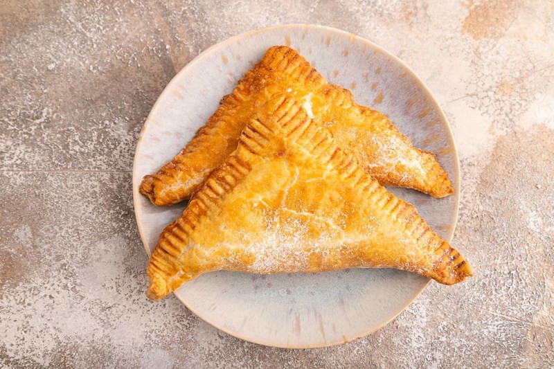 Triangles Pie, Puff Pastry, Samsa with cherry jam on brown concrete background, top view, flat lay, close up
