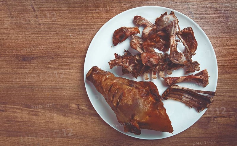 Roast pork head, with remnants of bones and meat, on a white platter, no people, close-up