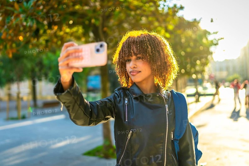 Latin young woman taking photos of the city using mobile phone during sunset