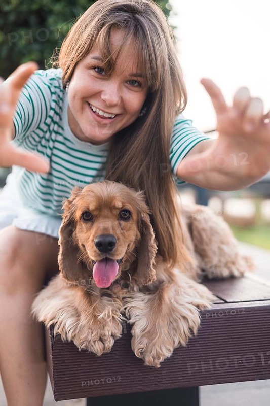 Joyful woman playfully posing with her dog Cocker Spaniel on a bench, expressing vitality