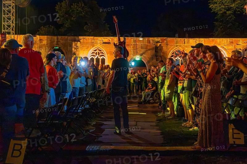 Artist walks with raised guitar through applauding audience at night concert, Calwer Klostersommer Festival, Hirsau Abbey, Calw, Germany