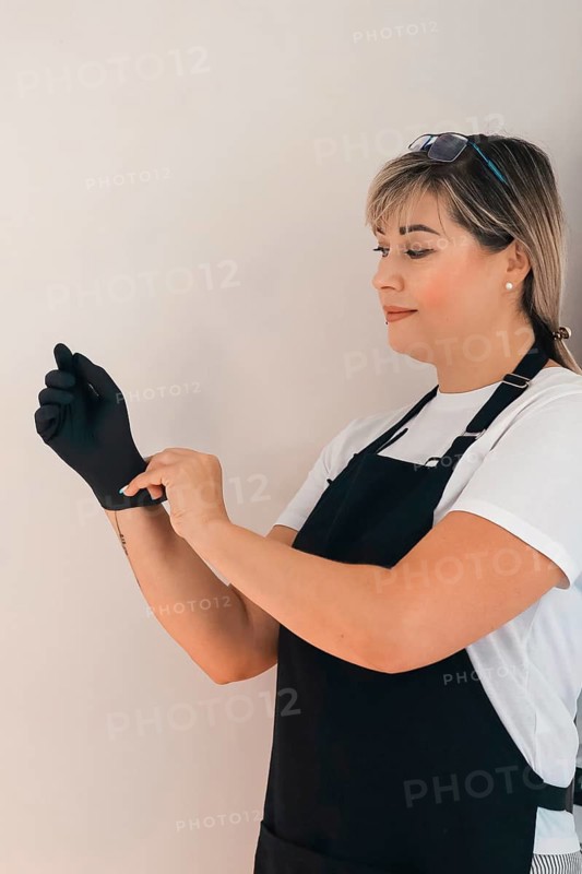 Woman putting on gloves, dressed in apron, minimalistic setting, focused